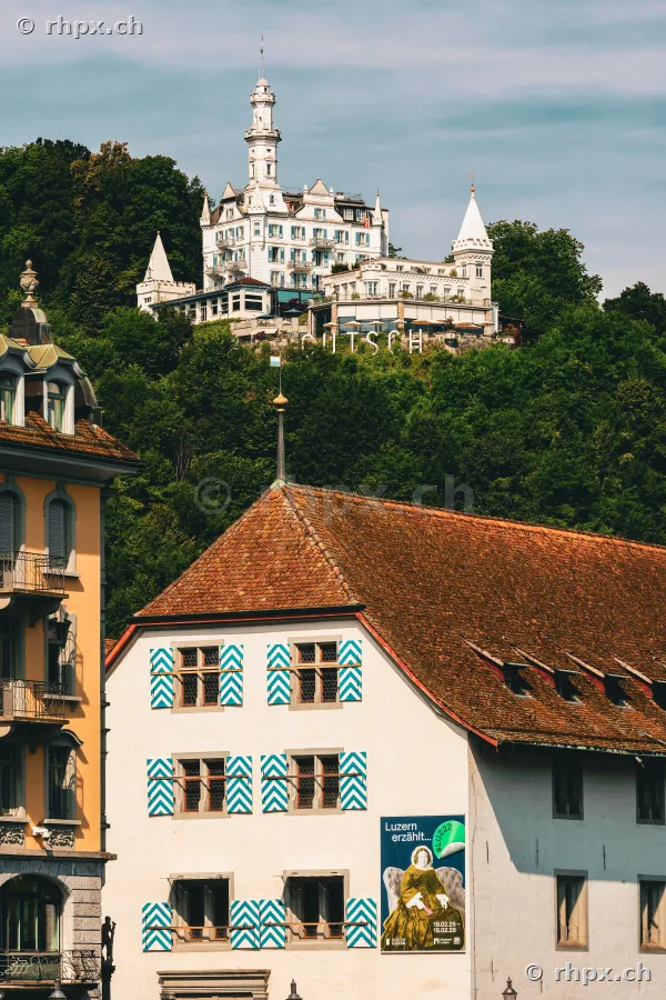 View of Hotel Château Gütsch on a wooded hill above historic buildings in Lucerne