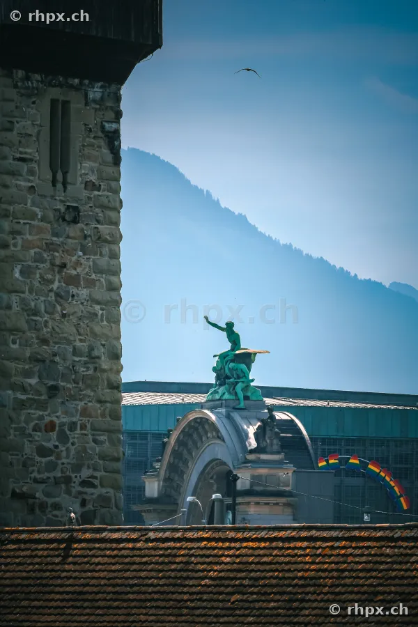 View of the Wasserturm and the sculpture on the Lucerne station in front of a mountain