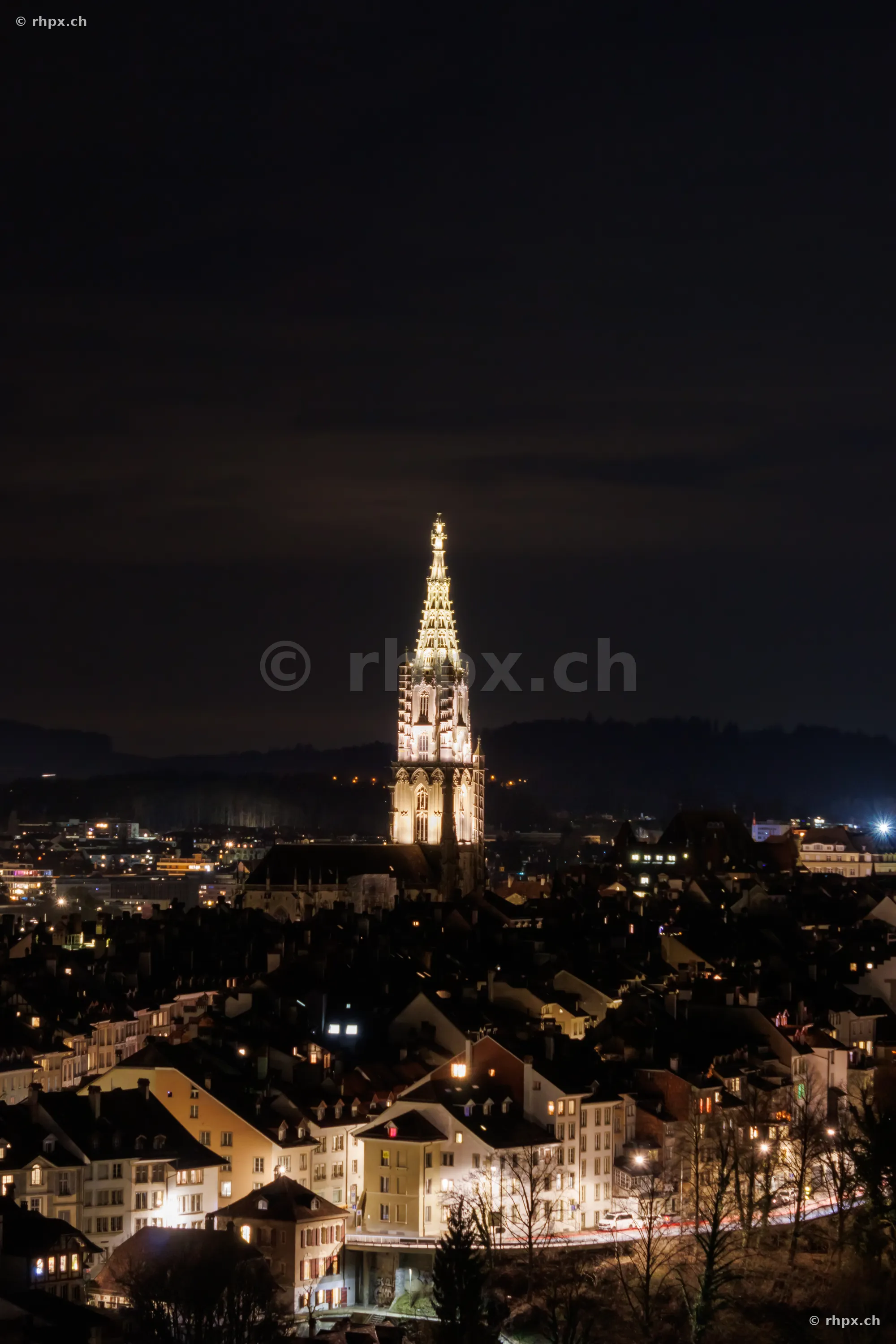 Ansicht des beleuchteten Berner Münsters über der nächtlichen Altstadt von Bern.