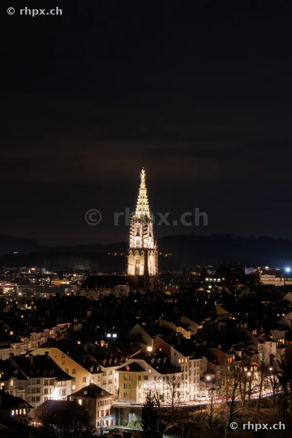 Ansicht des beleuchteten Berner Münsters über der nächtlichen Altstadt von Bern.