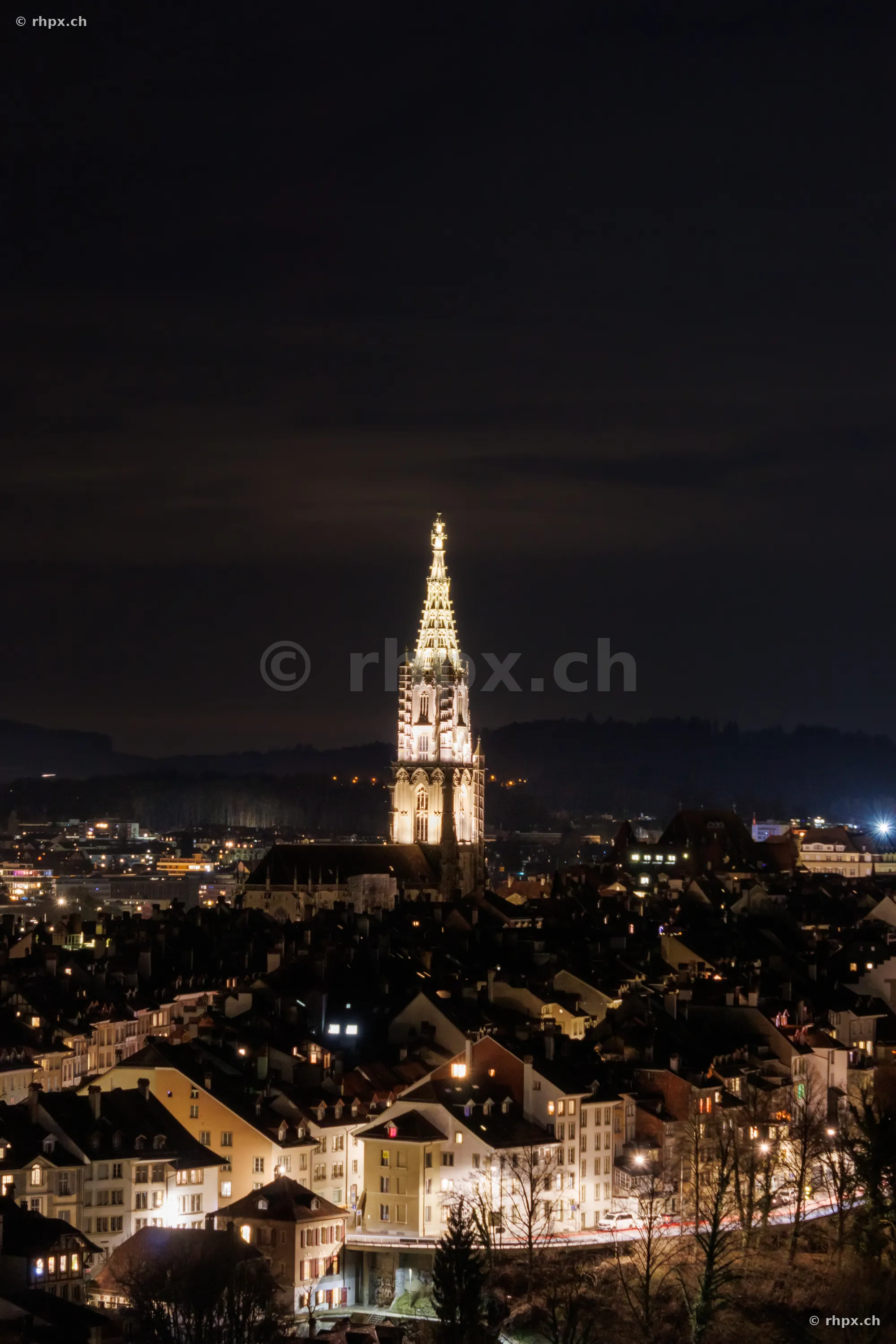 Der beleuchtete Turm des Berner Münsters über den Dächern der Altstadt bei Nacht