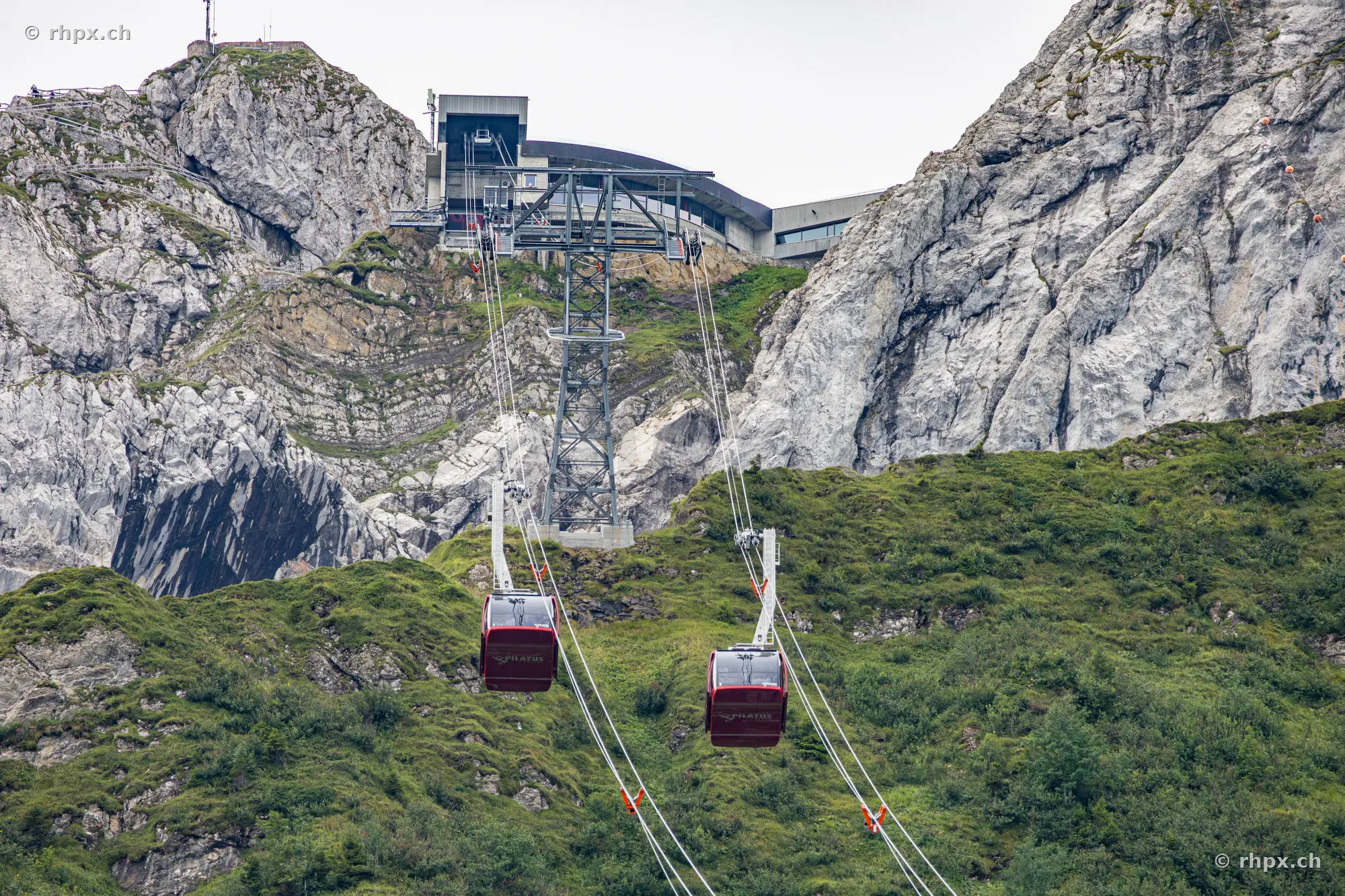 Two red cabins of the Dragon Ride aerial cableway at Mount Pilatus in front of rocky mountains