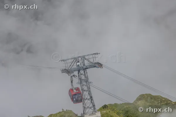 Rote Gondel der Pilatus-Luftseilbahn an einem Stahlmast in nebliger Berglandschaft