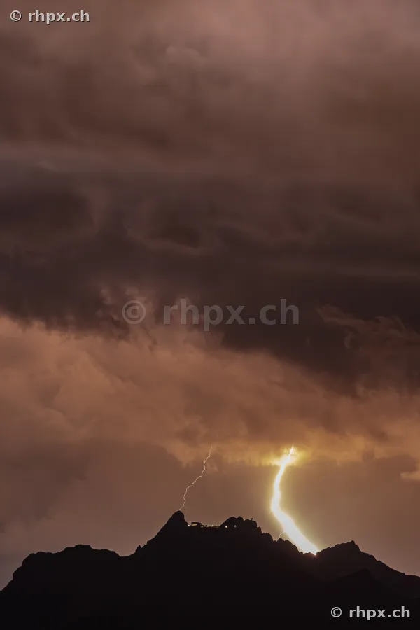 Ein heller Blitz entlädt sich in der Nacht über der dunklen Silhouette des Pilatusgipfels.