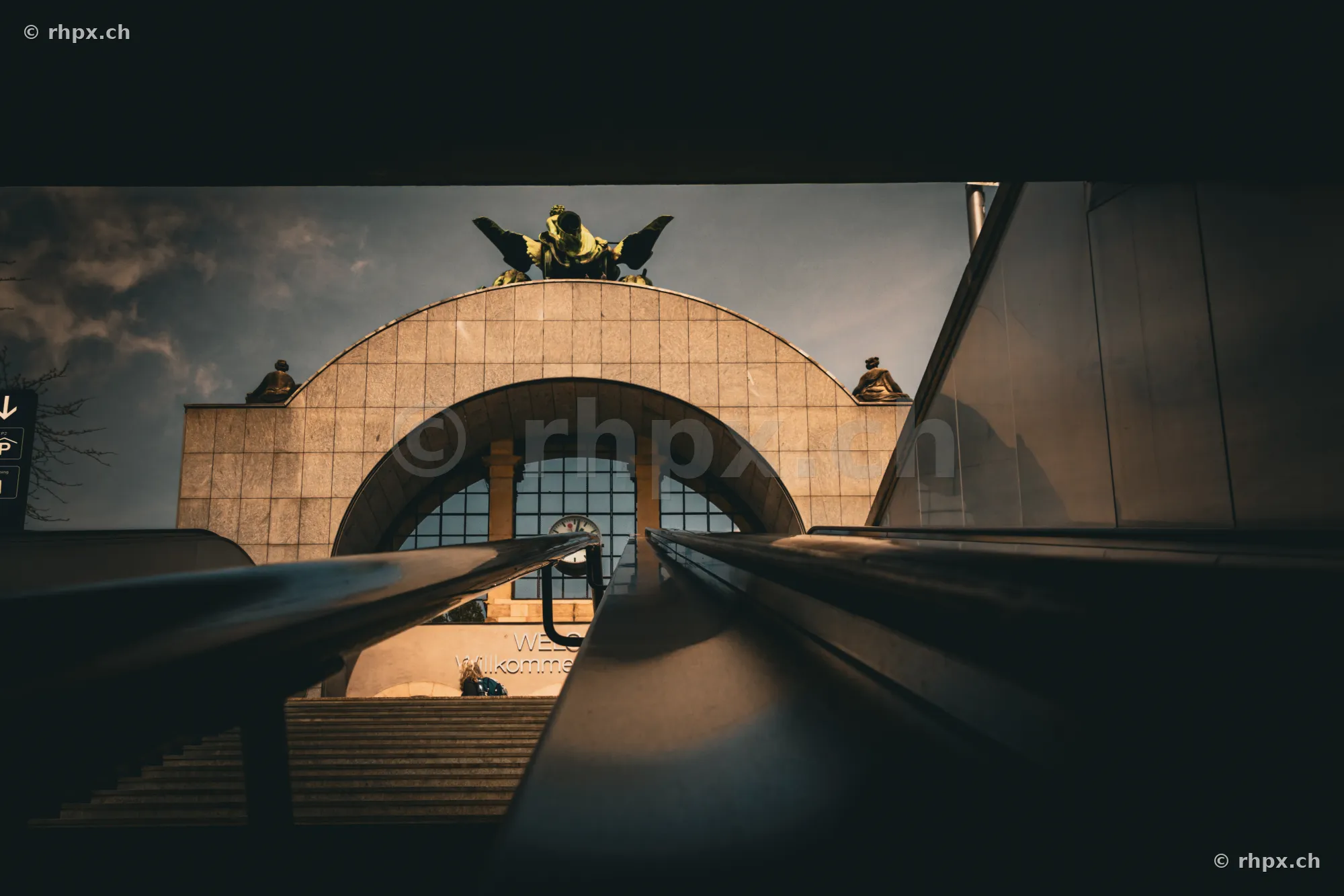 Portal of Lucerne train station featuring the sculpture by Hans Erni under a cloudy sky.