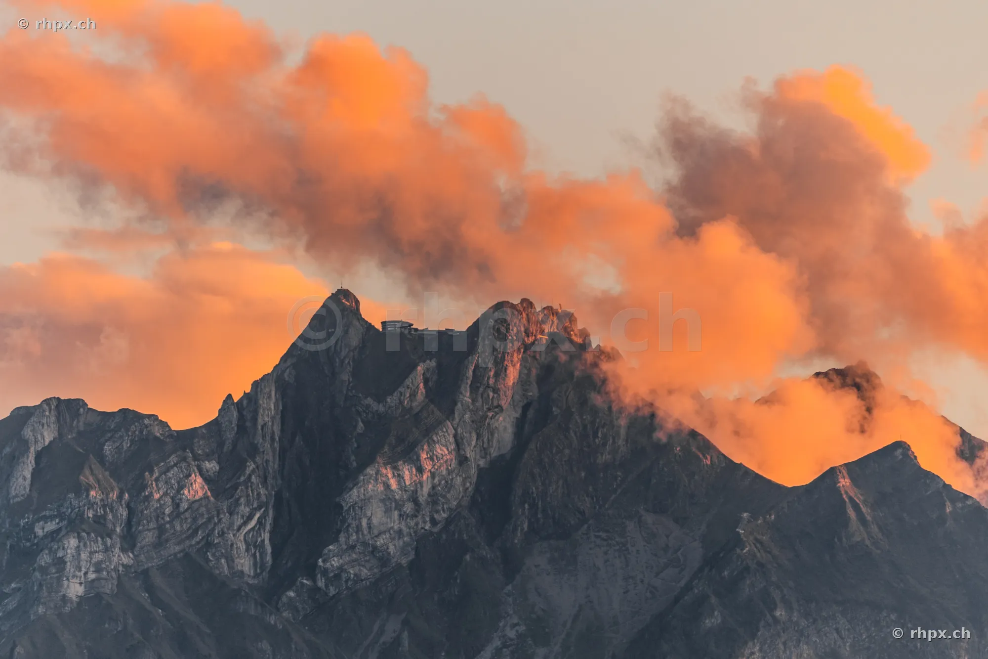 The summit of Mount Pilatus near Lucerne at dusk with orange-red illuminated clouds.