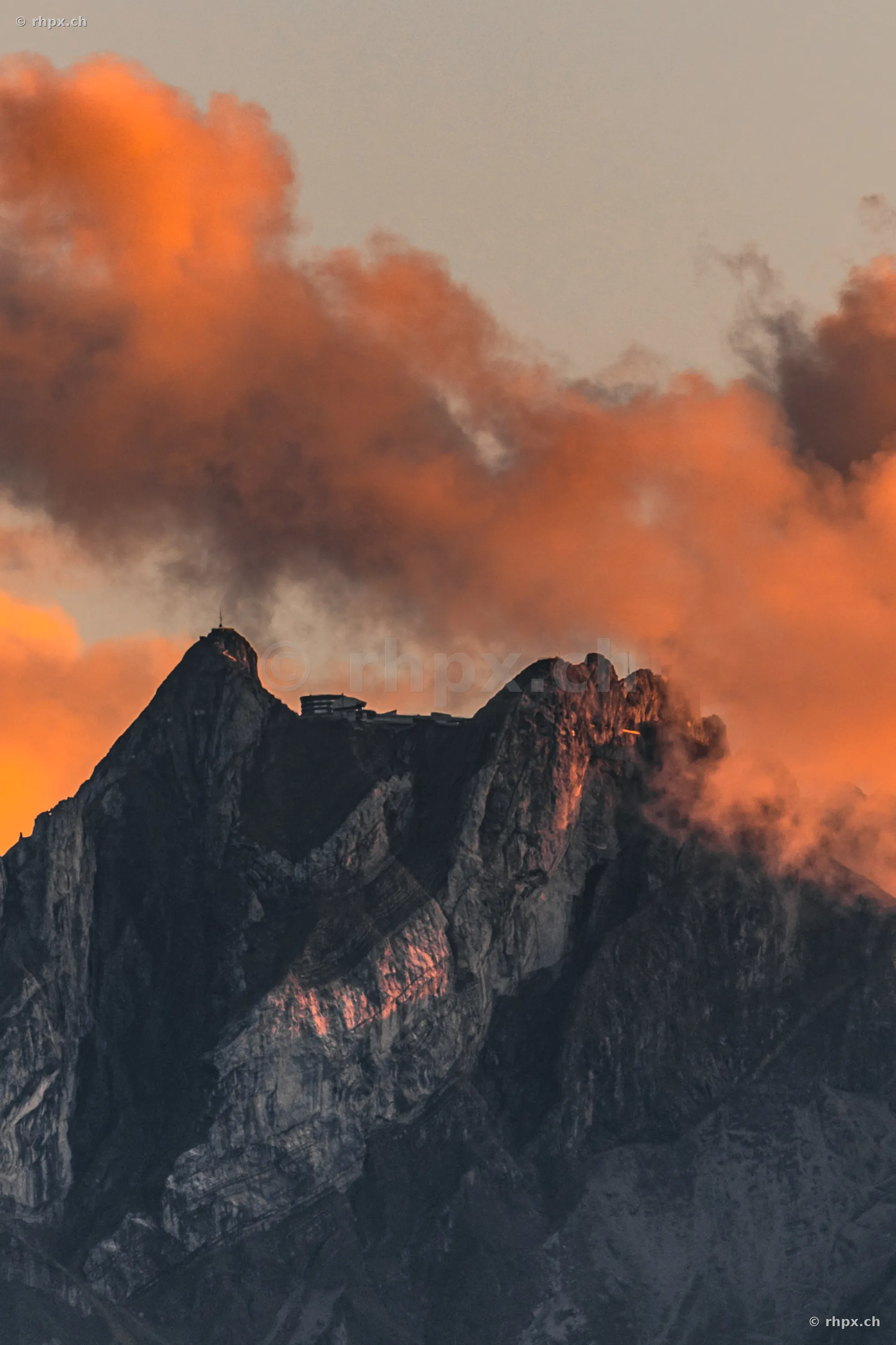 Rocky summit of Mount Pilatus near Lucerne with orange illuminated clouds at sunset