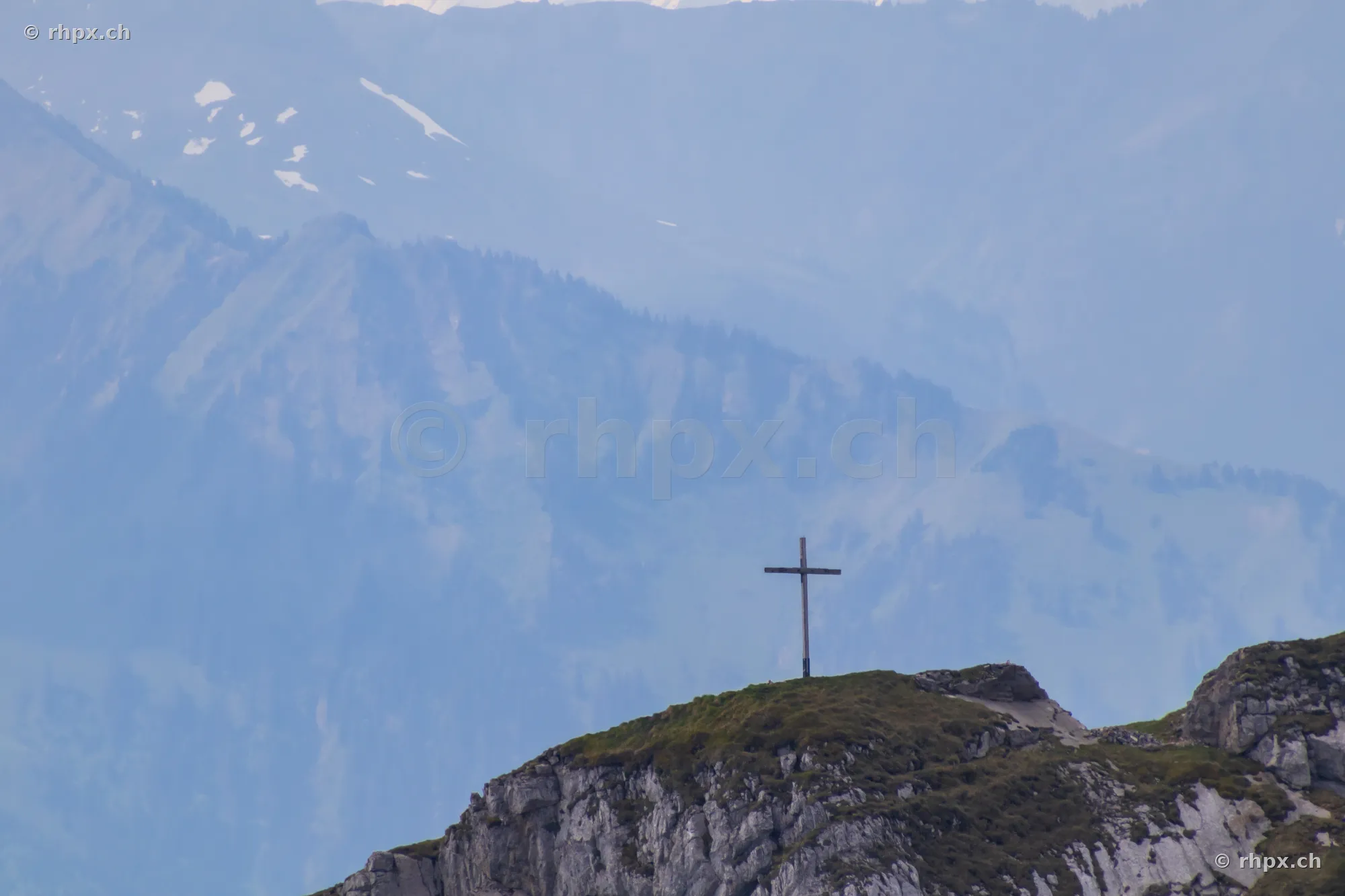 Gipfelkreuz auf einer felsigen Erhebung des Pilatus mit verschneiten Bergen im Hintergrund