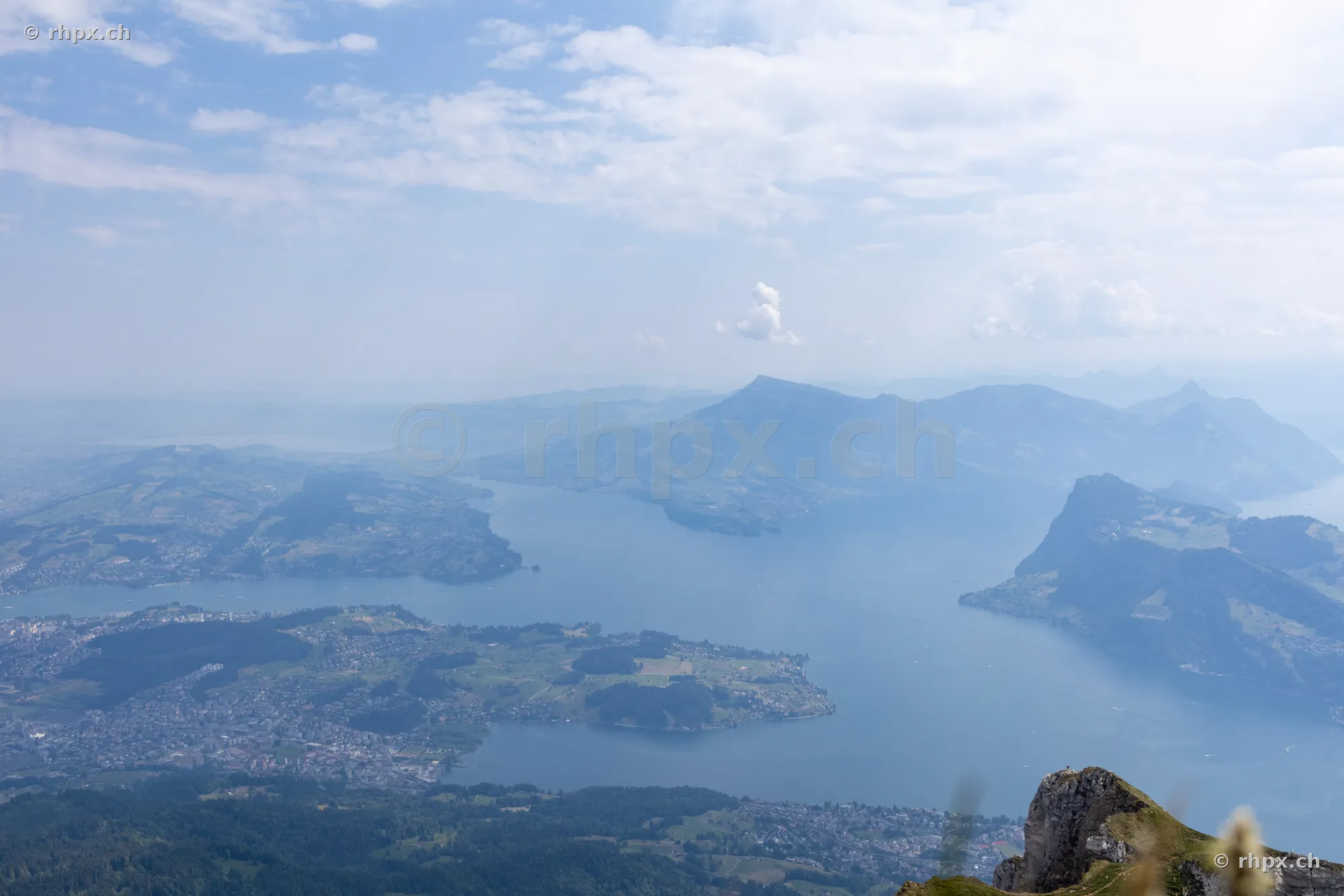 View from the height of Mount Pilatus looking over Lake Lucerne and the surrounding mountain landscape in daylight.