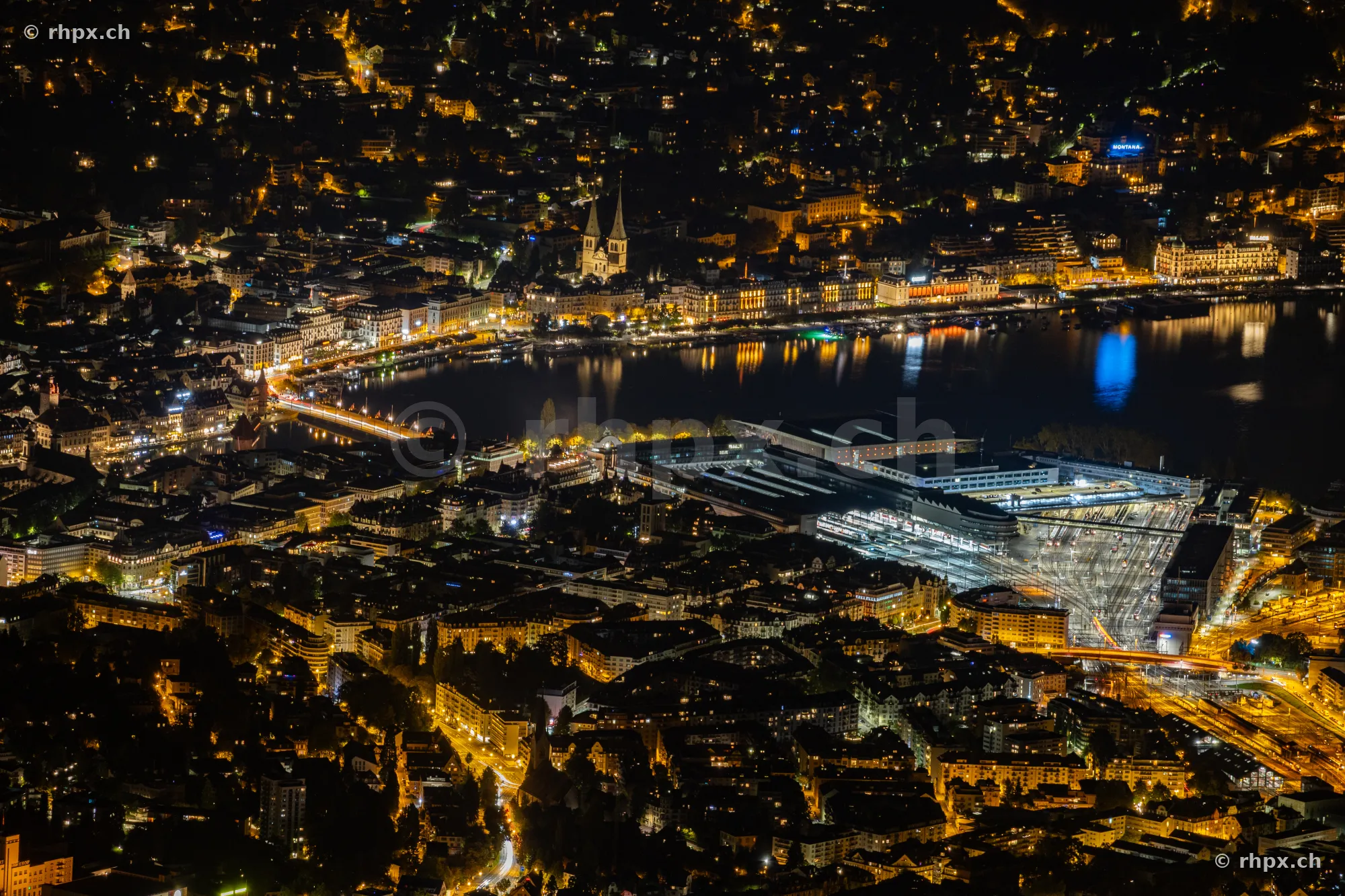 Nächtliche Luftaufnahme der Stadt Luzern mit See, Bahnhof und Hofkirche, fotografiert vom Pilatus aus.