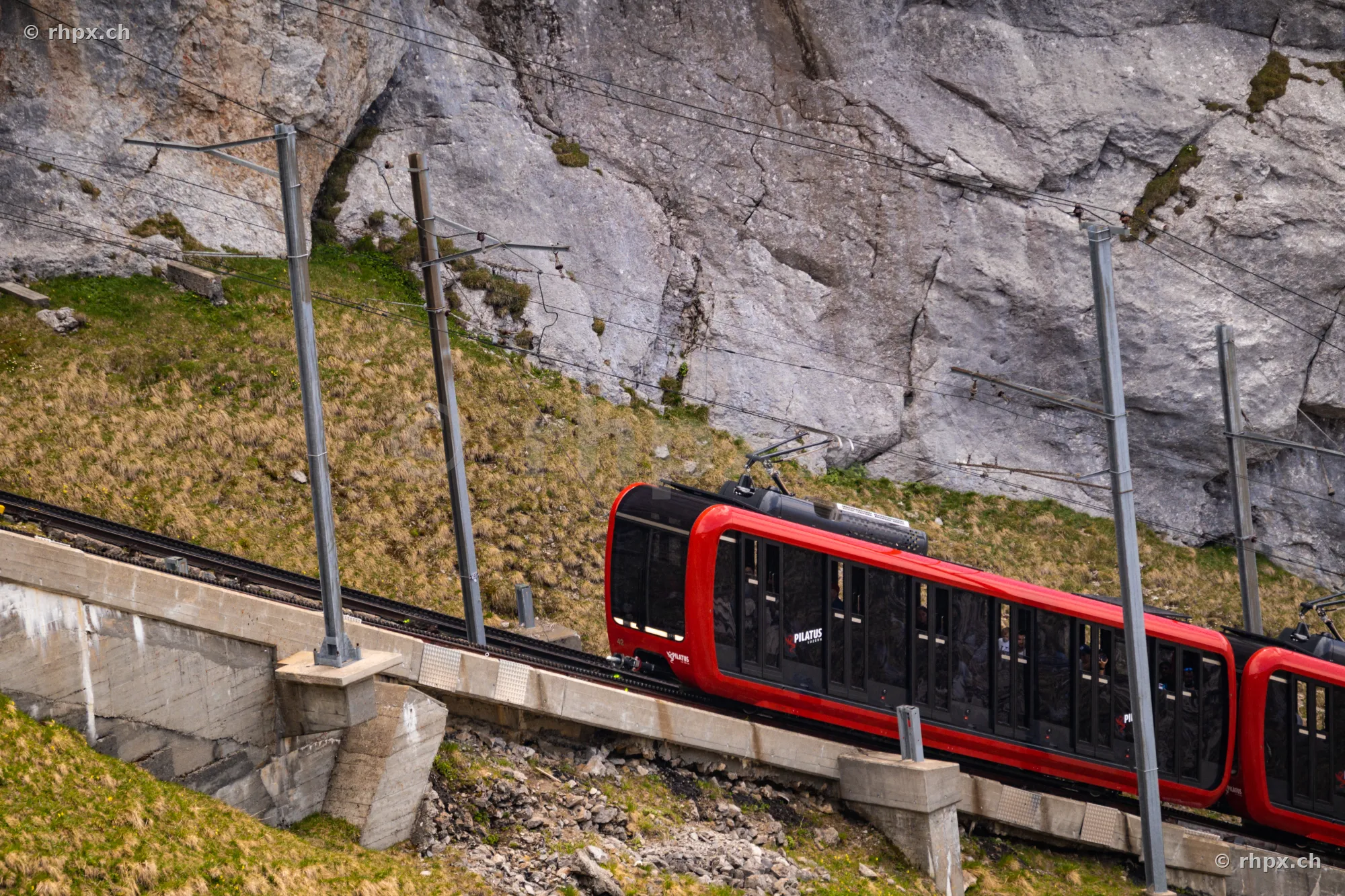 Die rote Pilatusbahn fährt auf ihrer steilen Strecke vor einer Felswand.