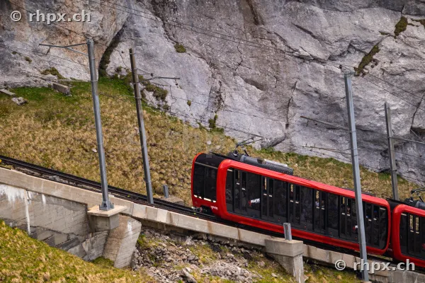 Die rote Pilatusbahn fährt auf ihrer steilen Strecke vor einer Felswand.