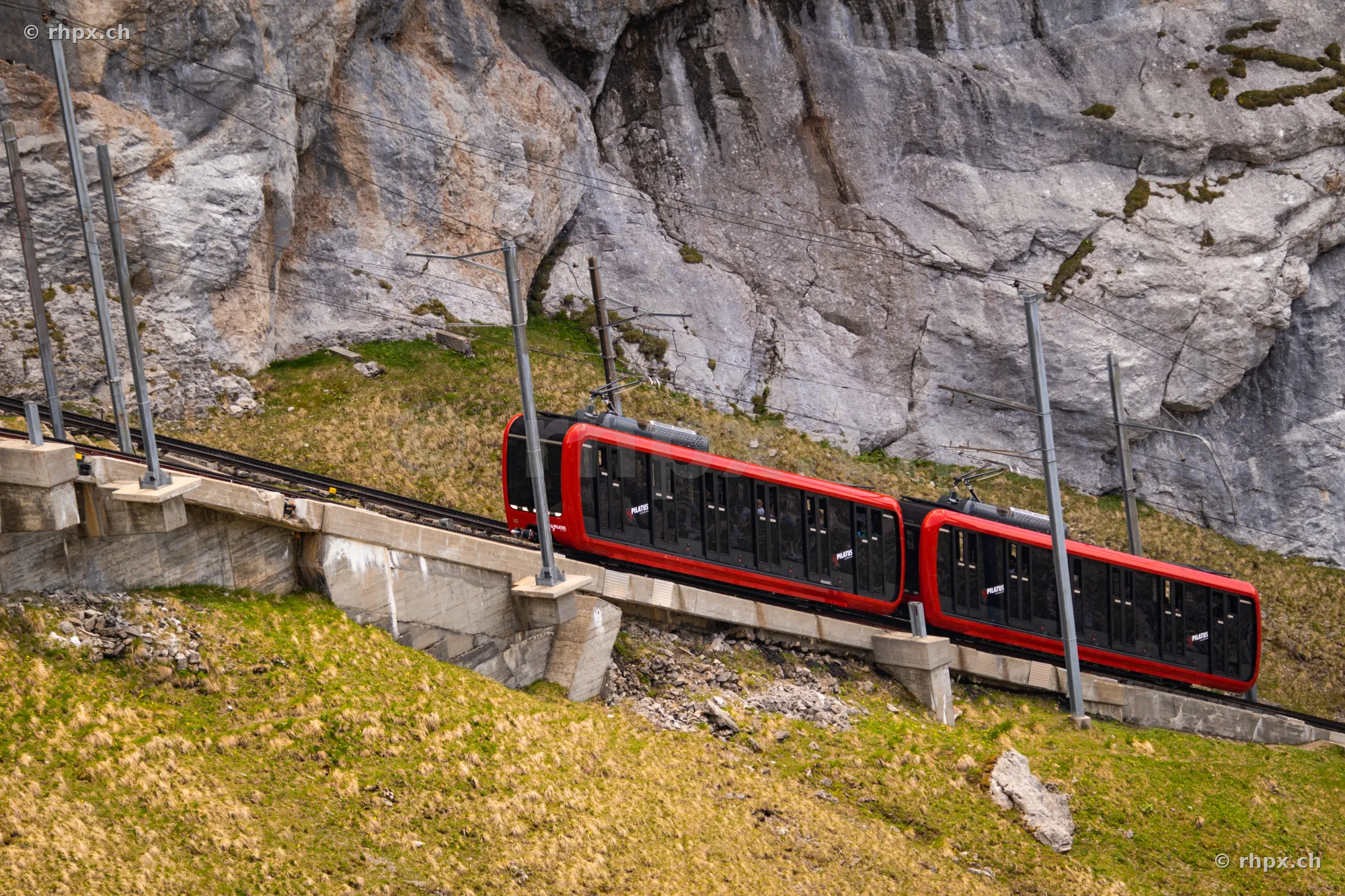 Red railcar of the Pilatus cogwheel railway driving through a steep rock face