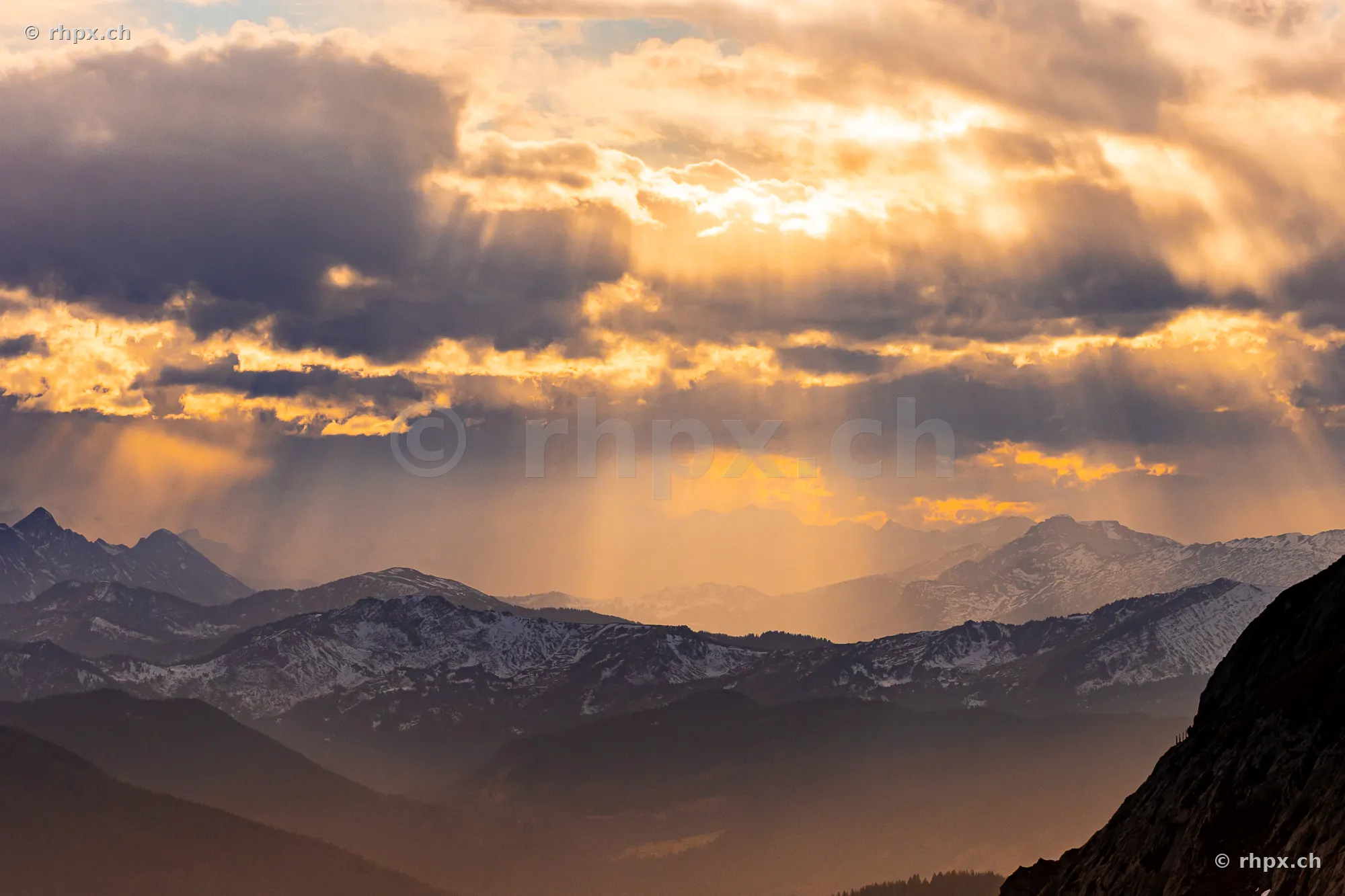 Evening sun rays breaking through clouds over the snow-covered peaks of Mount Pilatus