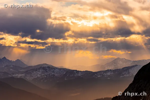 Evening sun rays breaking through clouds over the snow-covered peaks of Mount Pilatus