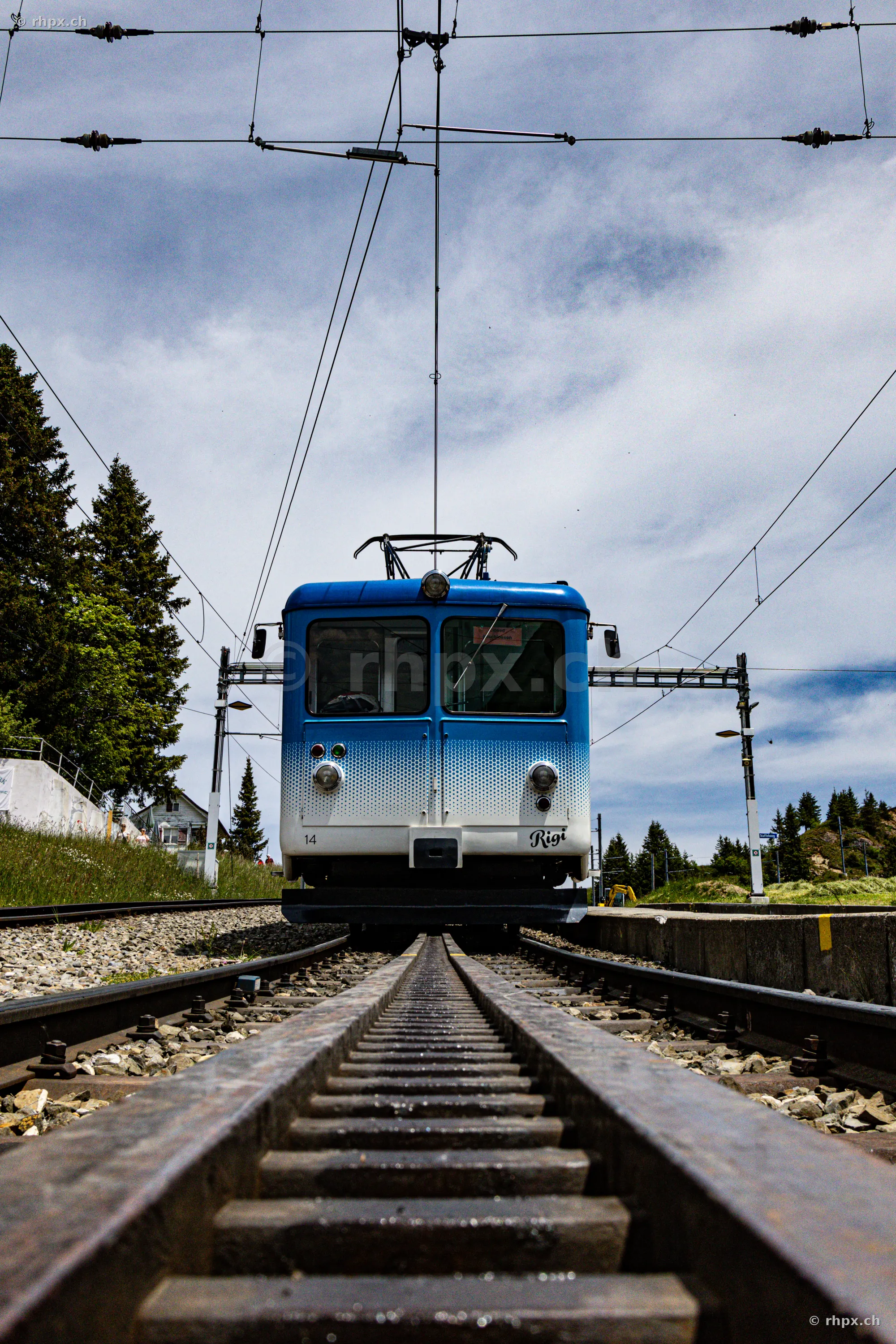 Ein blau-weisser Triebwagen der Rigi-Zahnradbahn steht auf den Gleisen vor einem Bahnhof.