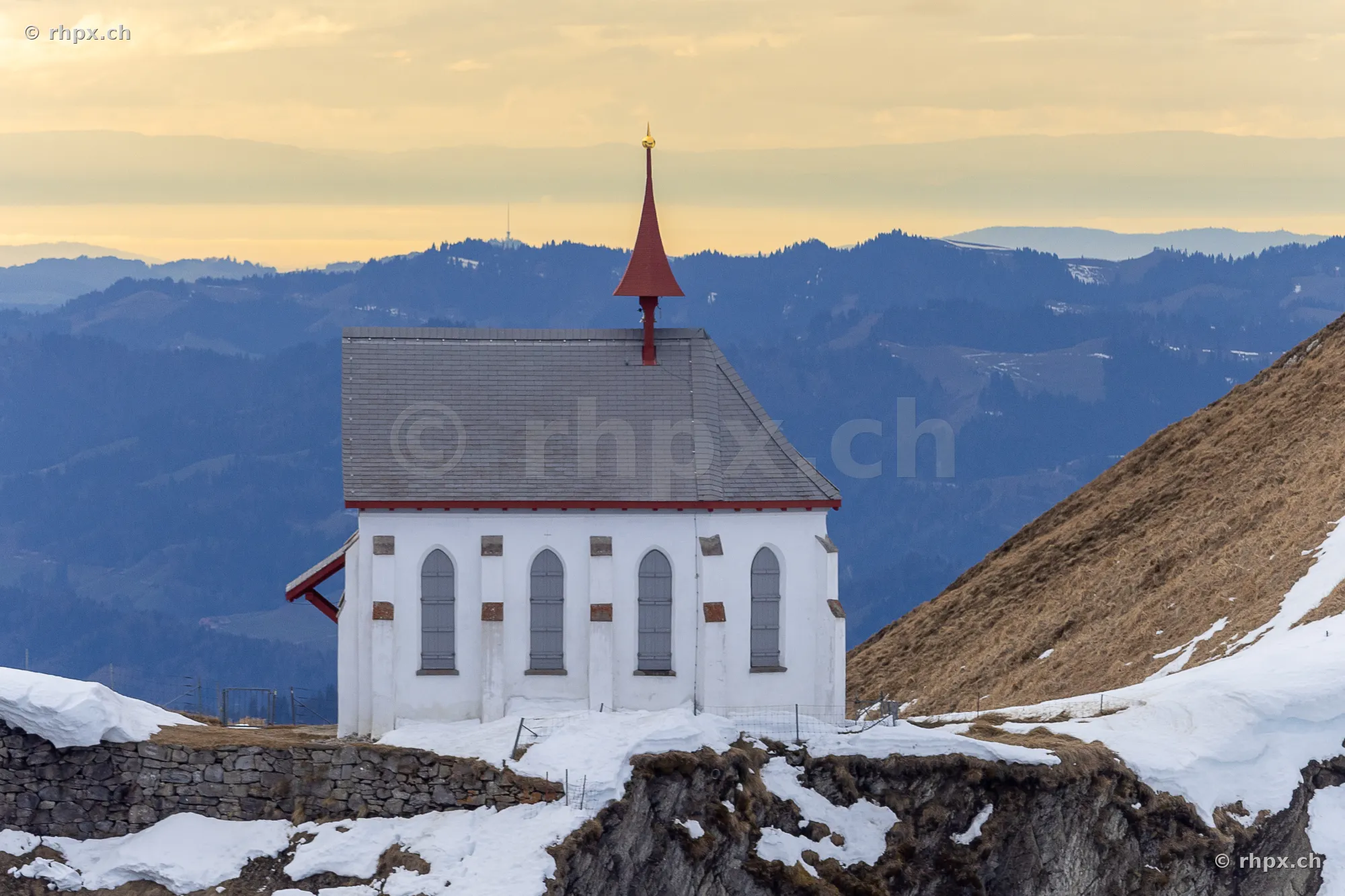 White chapel in front of the Mount Pilatus mountain panorama with snow patches
