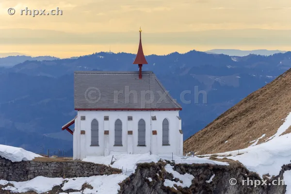 White chapel in front of the Mount Pilatus mountain panorama with snow patches