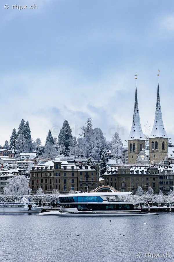 Lake Lucerne with a modern passenger boat in front of the snow-covered Hofkirche in Lucerne