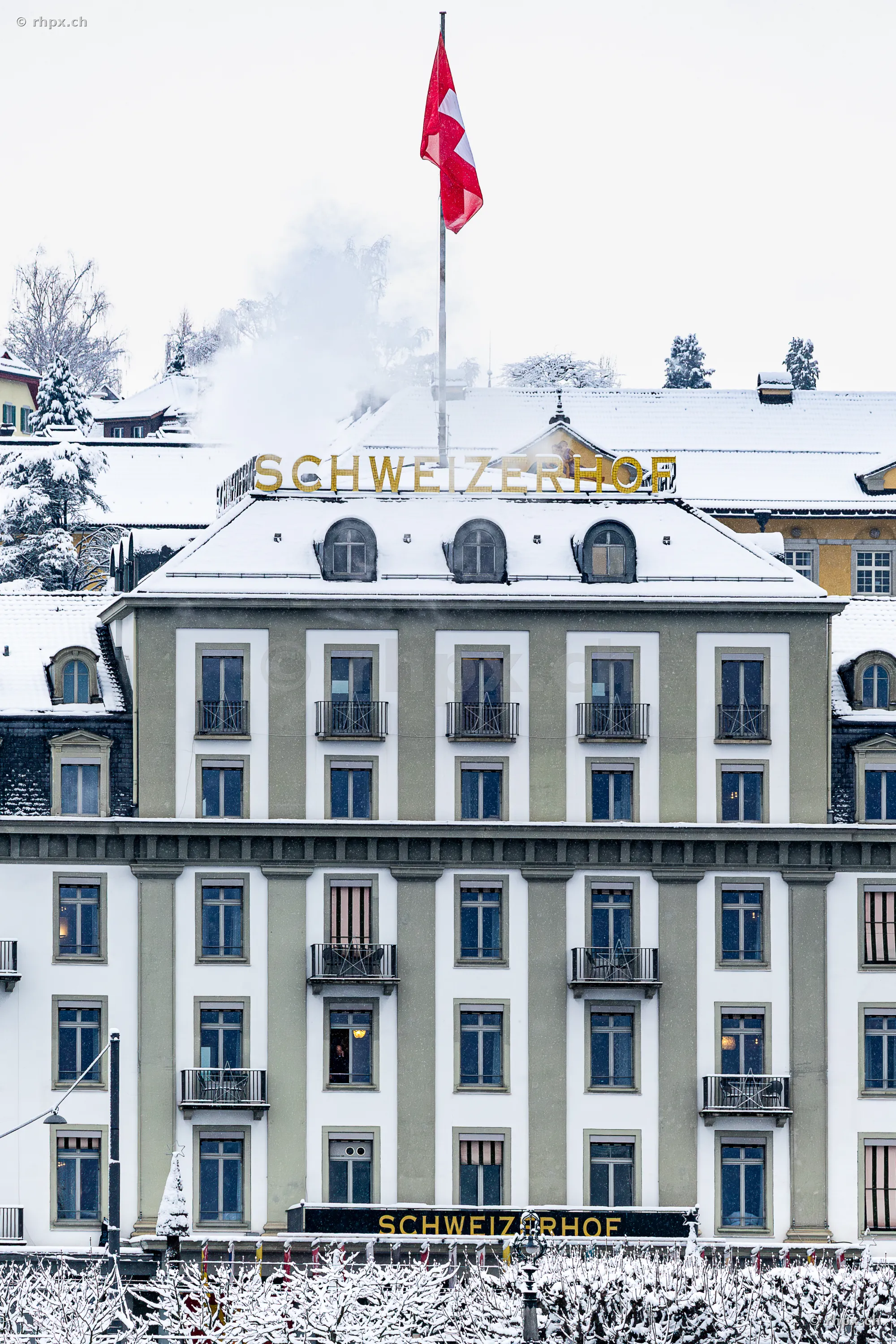 Die verschneite Fassade des Hotel Schweizerhof in Luzern mit wehender Schweizer Flagge.