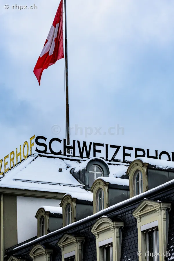 Schneebedecktes Dach des Hotels Schweizerhof in Luzern mit wehender Schweizer Fahne