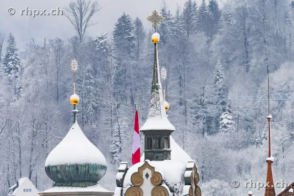 Close-up of the snow-covered onion domes of the Jesuit Church in Lucerne in front of a wooded hillside.