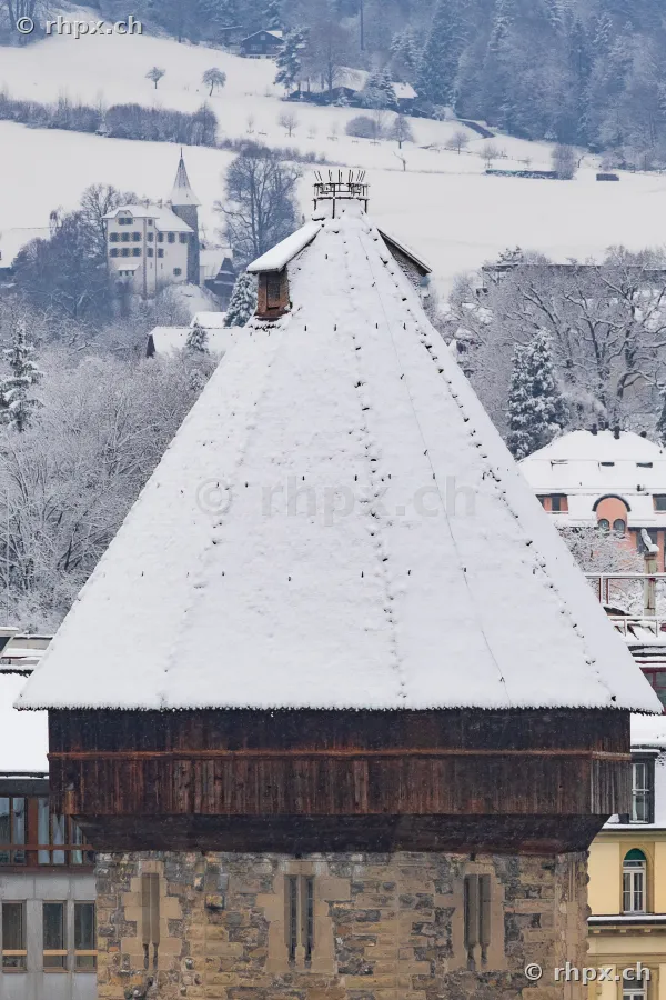Close-up of a snow-covered Musegg Wall tower in Lucerne against a winter landscape background