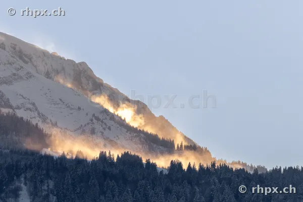 Verschneiter Berghang des Pilatus im goldenen Licht mit Wald und Nebelschwaden