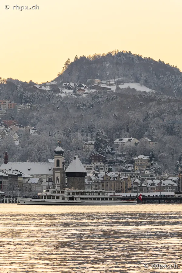 A passenger boat on Lake Lucerne in front of the snow-covered city of Lucerne in the evening light
