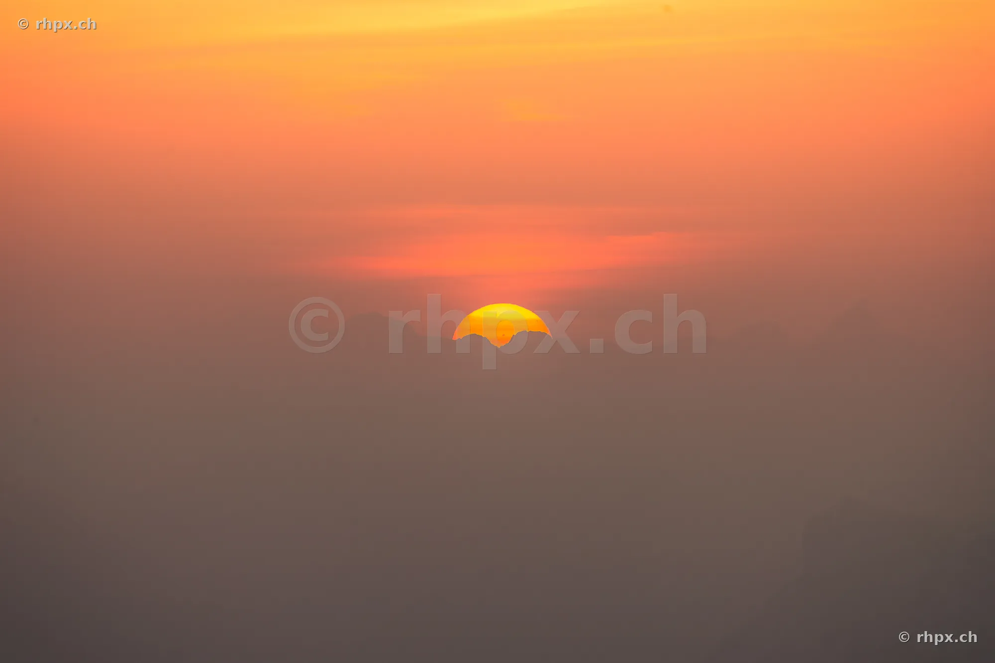 The sun sets behind the silhouette of Mount Pilatus in a sea of fog.