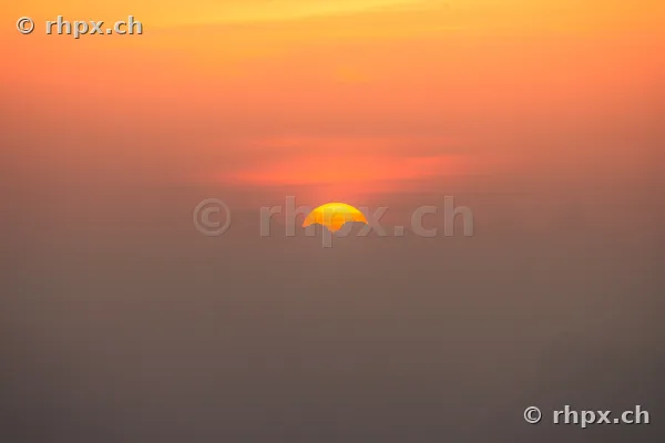 Die Sonne geht hinter der Silhouette des Pilatus in einem Nebelmeer unter.