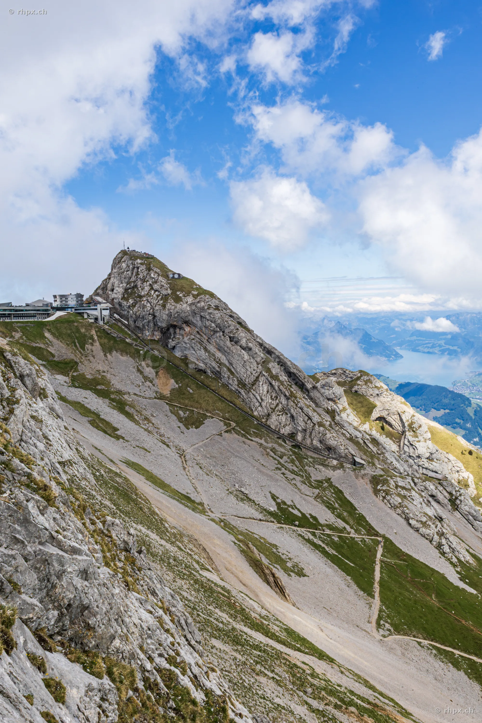 View of the Pilatus summit rock formation with the hotel building and mountain station in daylight.