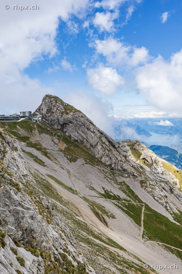 Blick auf die Felsformation des Pilatus-Gipfels mit Hotelgebäude und Bergstation bei Tageslicht.