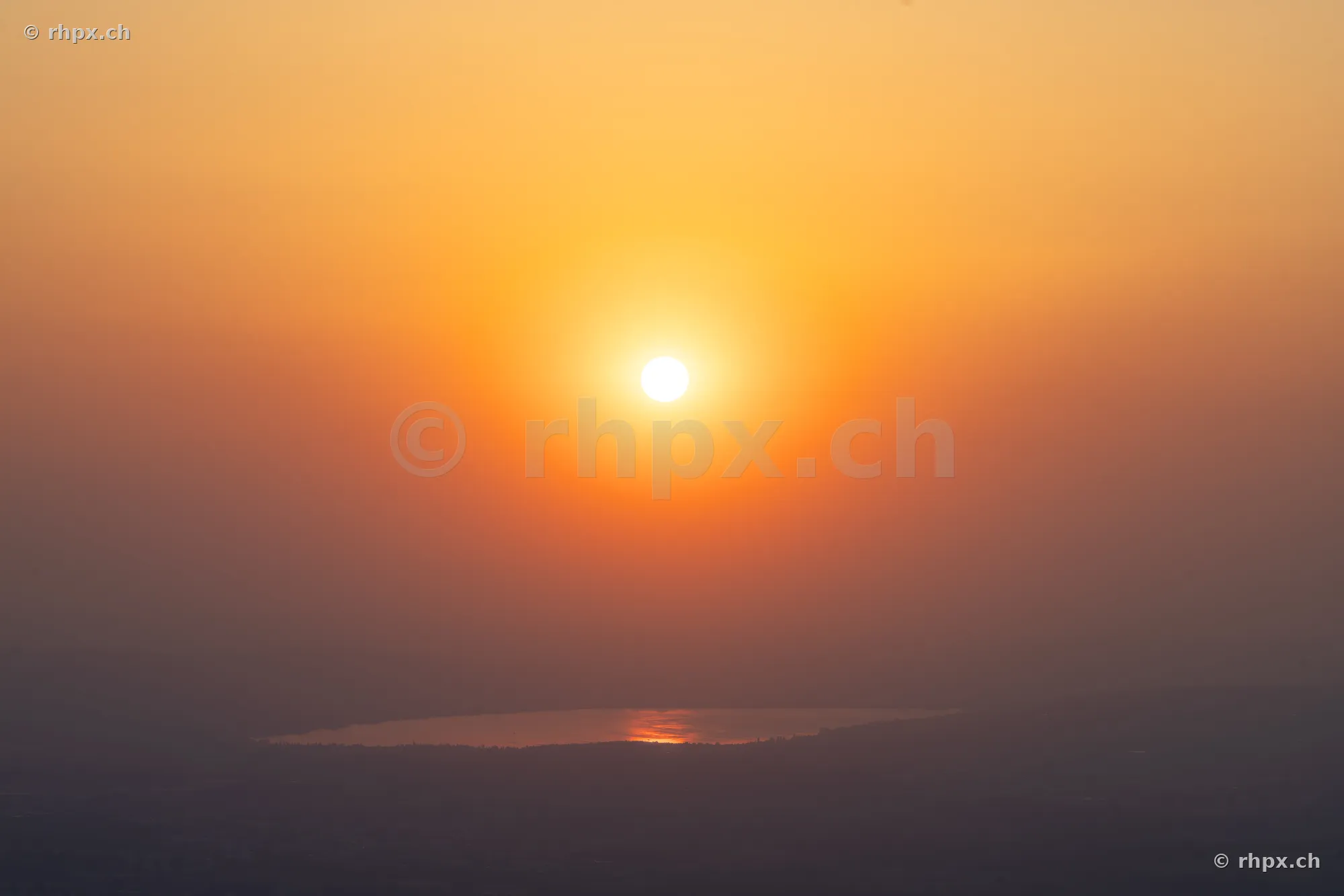 Tiefstehende Sonne über dem Baldeggersee in orange-gelbem Licht durch Saharastaub
