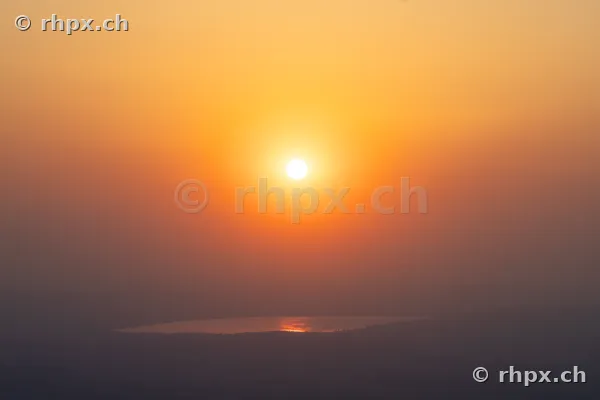 Low sun over Lake Baldegg in orange-yellow light due to Saharan dust