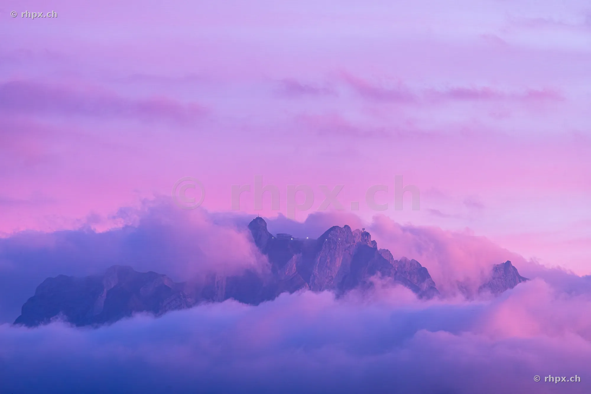 Der in Wolken gehüllte Gipfel des Pilatus bei violettem Licht in der Abenddämmerung.
