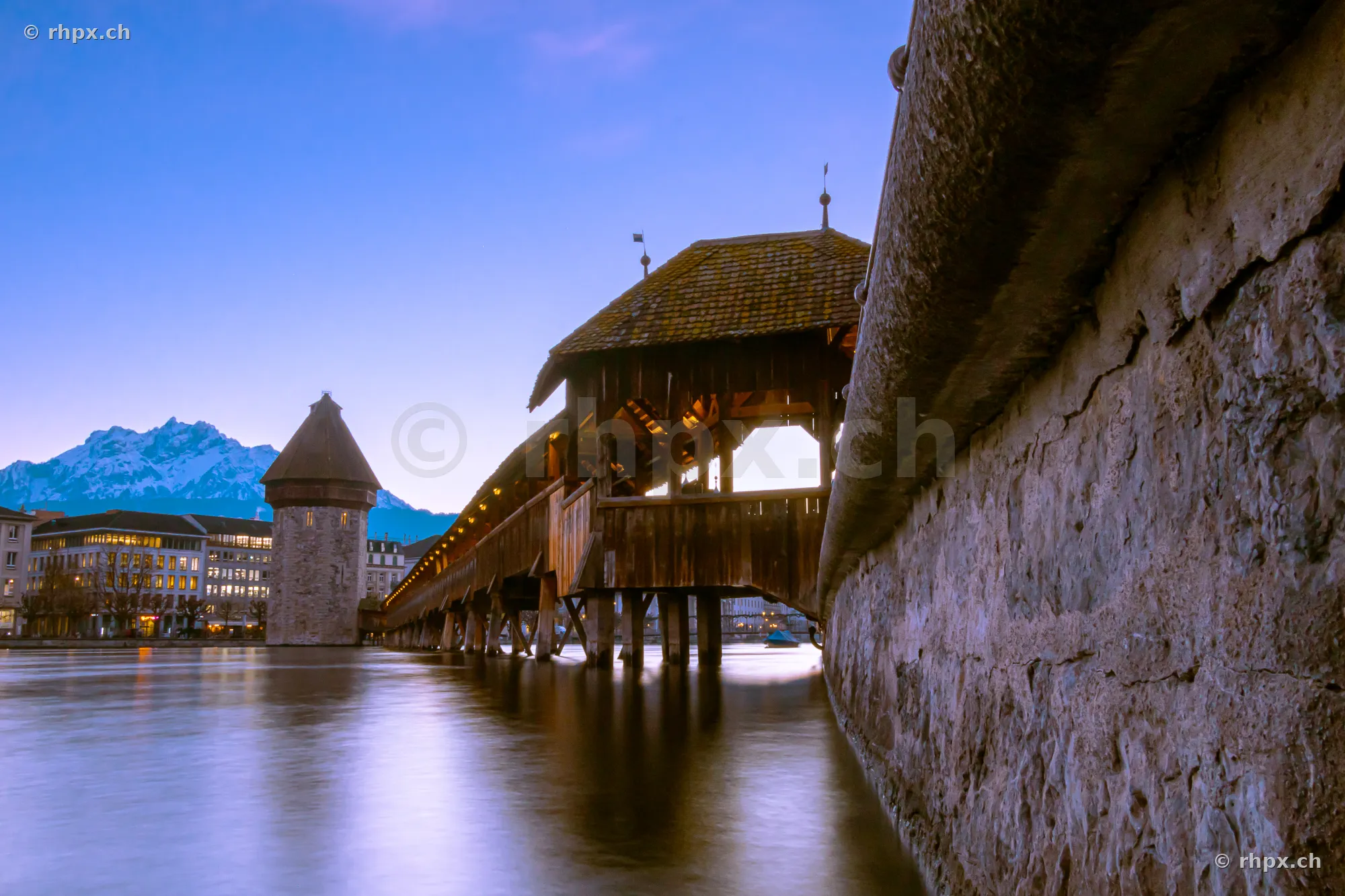 View along the Chapel Bridge and Water Tower in Lucerne at twilight with Mount Pilatus in the background
