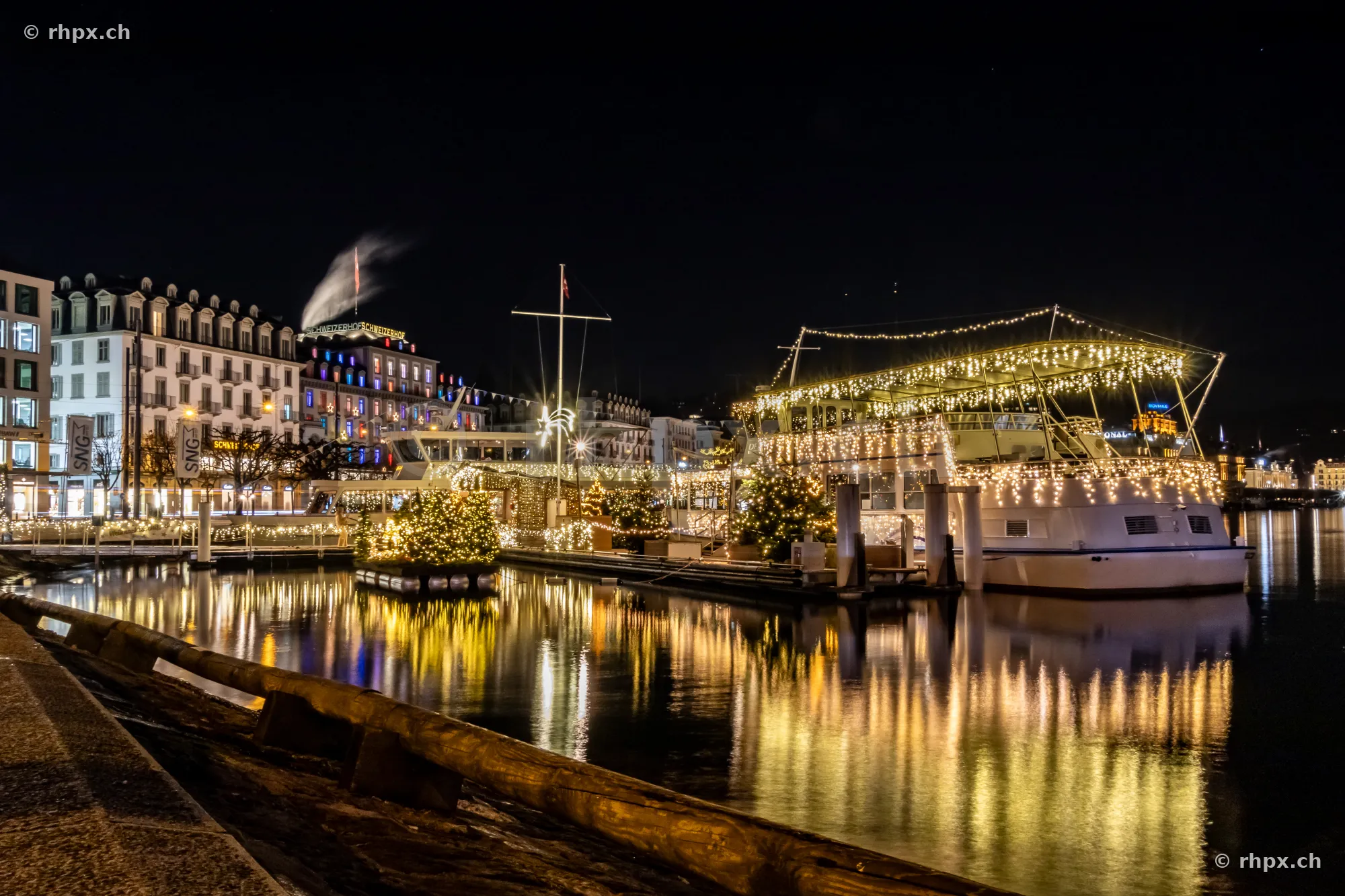 A Christmas-lit passenger boat moored at the Lucerne quay at night.