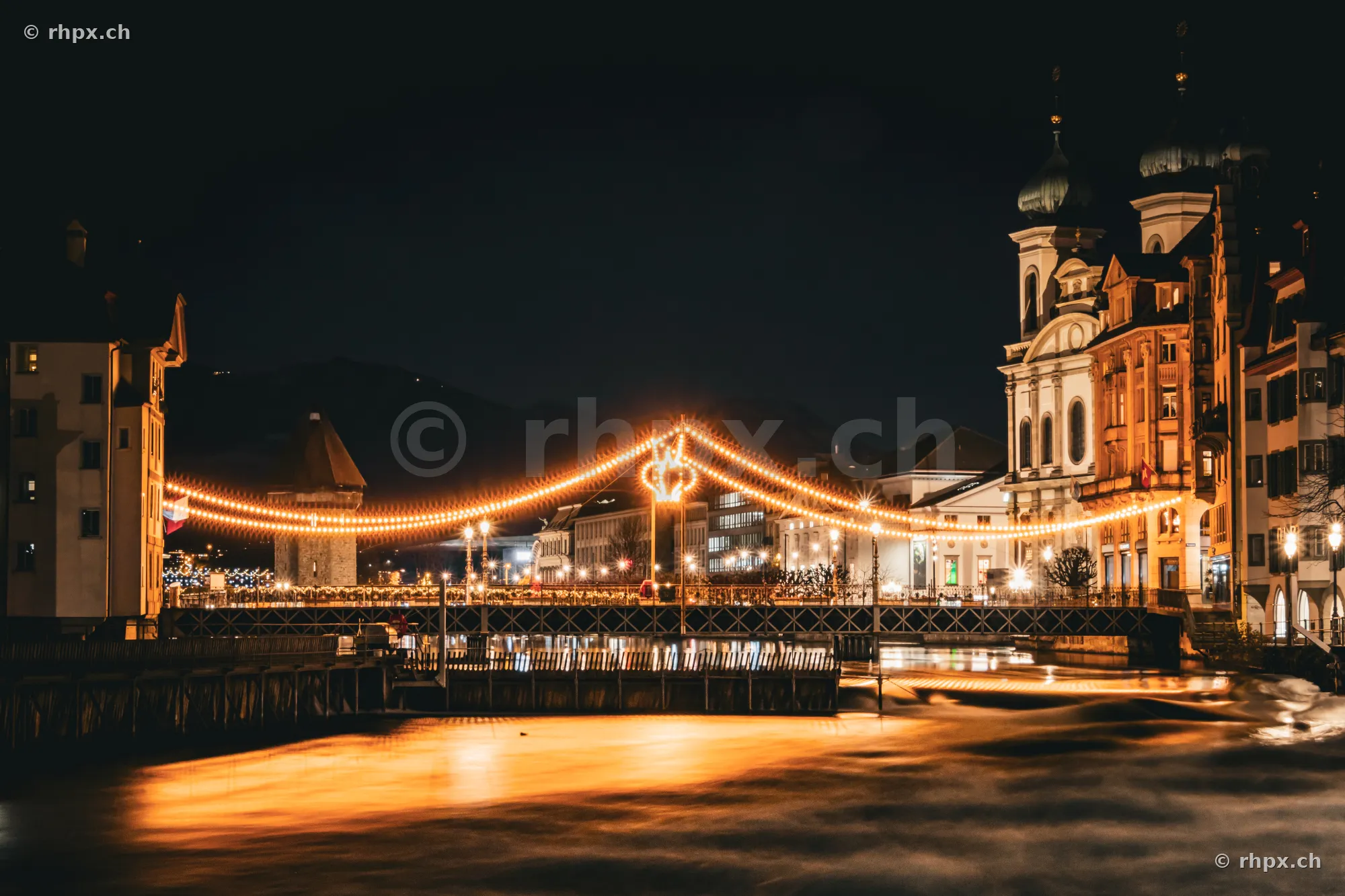 Rathaussteg in Lucerne at night with festive lights and view of the Jesuit Church