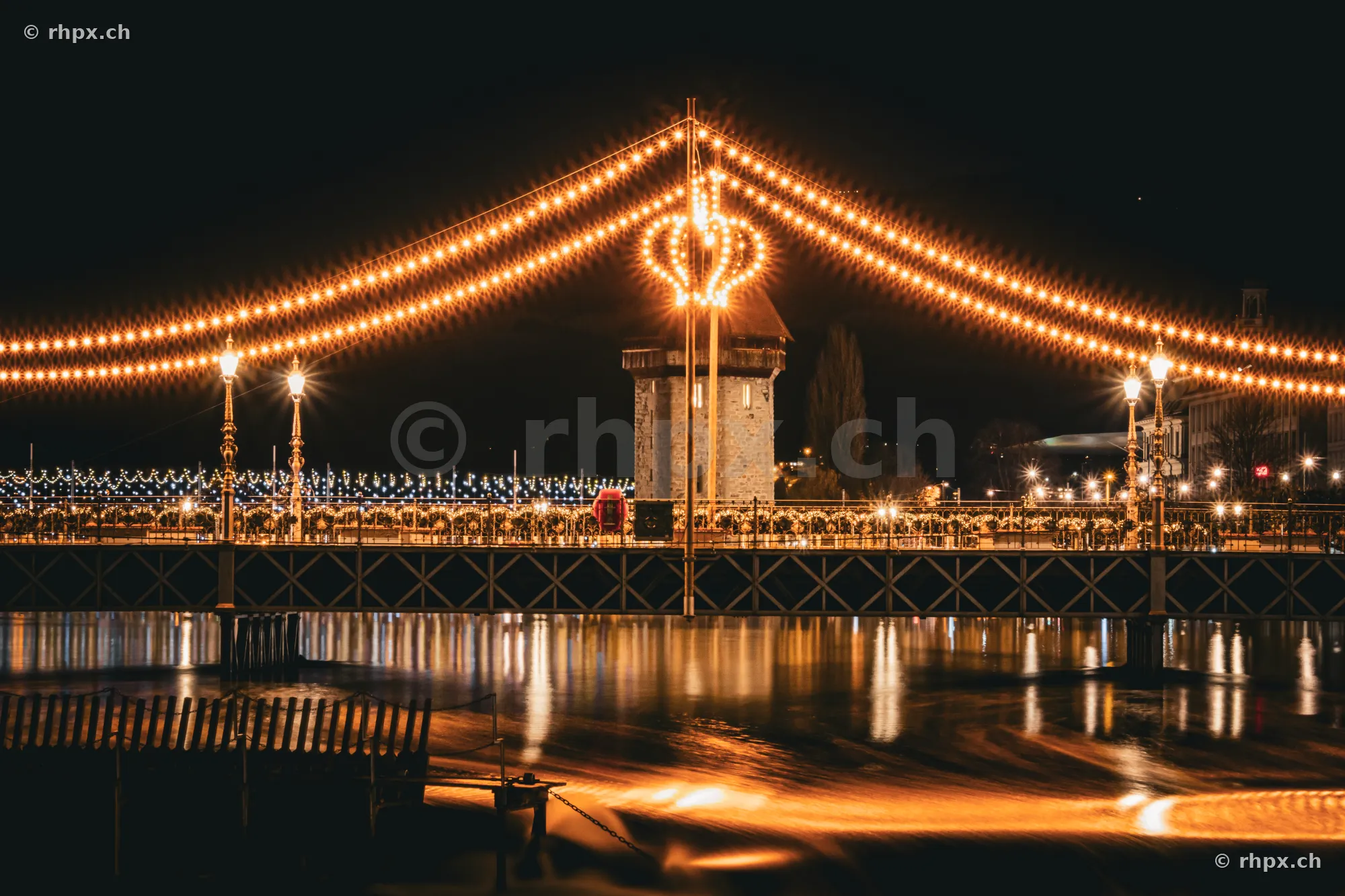Christmas-lit Seebrücke bridge in Lucerne at night with the Water Tower in the background
