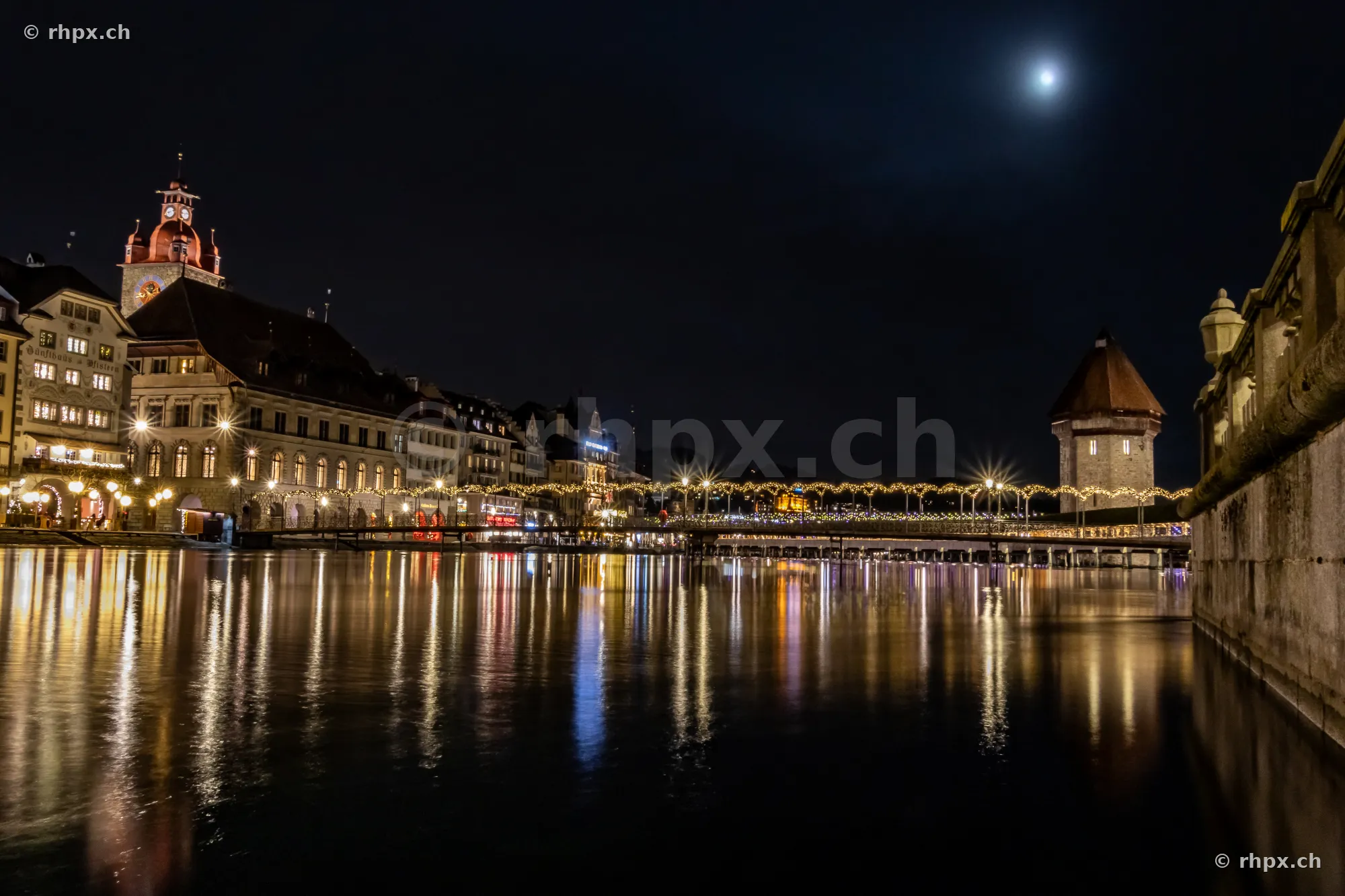 Night view of the Christmas-illuminated Reuss bridge and the water tower in Lucerne.