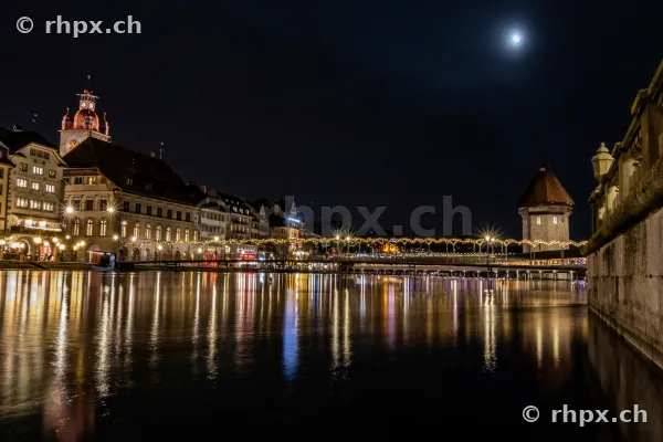 Nächtlicher Blick auf die weihnachtlich beleuchtete Reussbrücke und den Wasserturm in Luzern.