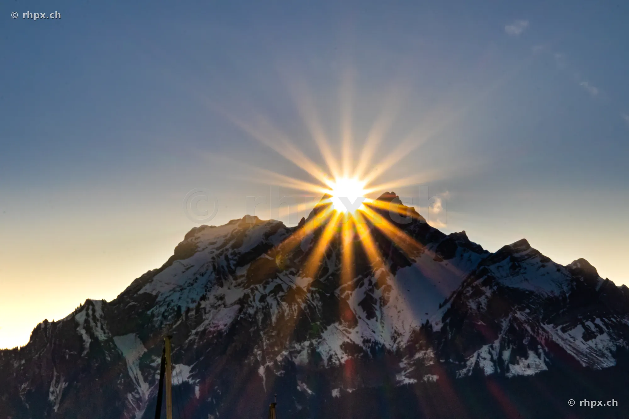The sun rises directly behind the jagged peak of the snow-covered Pilatus mountain.
