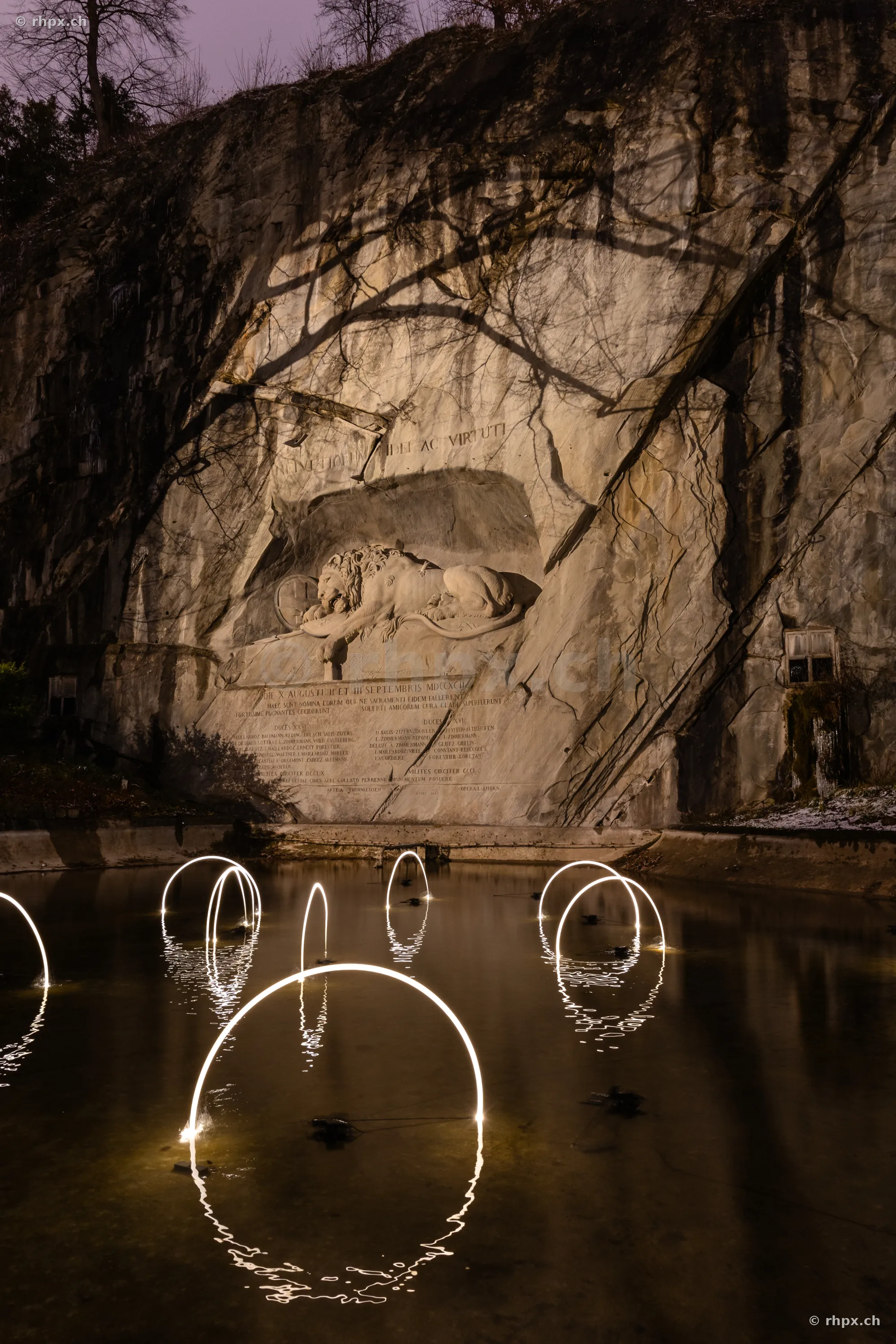 Das Löwendenkmal in Luzern bei Nacht mit Lichtinstallationen des Lilu Lichtfestivals im vorgelagerten Weiher