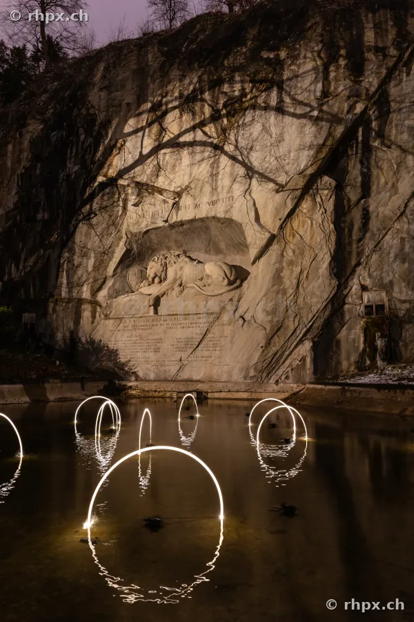 Das Löwendenkmal in Luzern bei Nacht mit Lichtinstallationen des Lilu Lichtfestivals im vorgelagerten Weiher