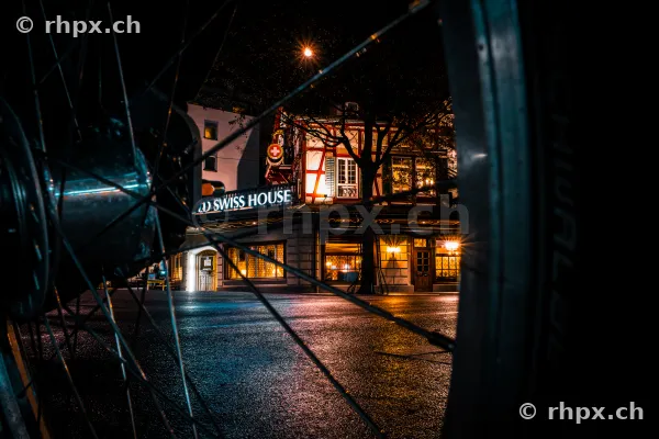 View through a bicycle wheel of the illuminated Swiss House in Lucerne at night