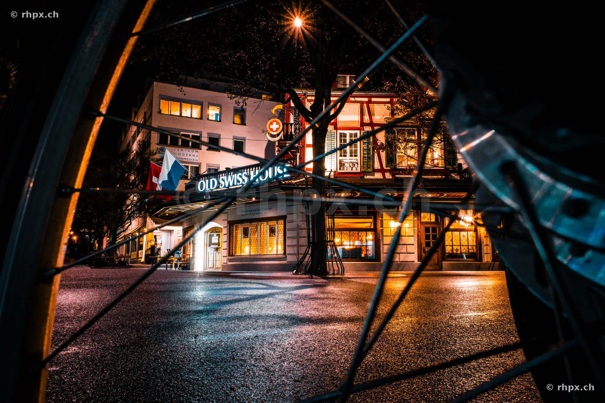The Old Swiss House in Lucerne at night, viewed through a bicycle wheel