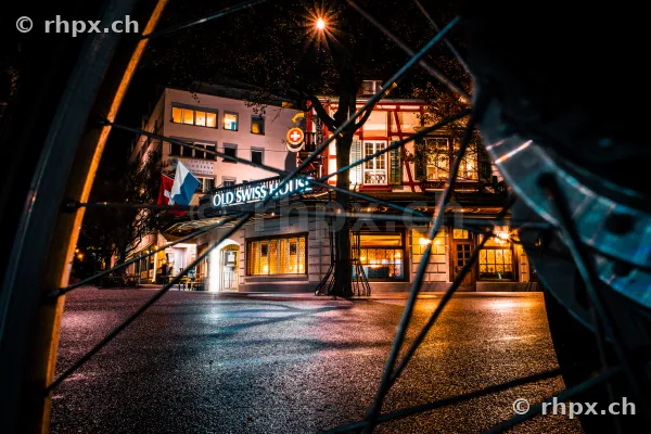 The Old Swiss House in Lucerne at night, viewed through a bicycle wheel