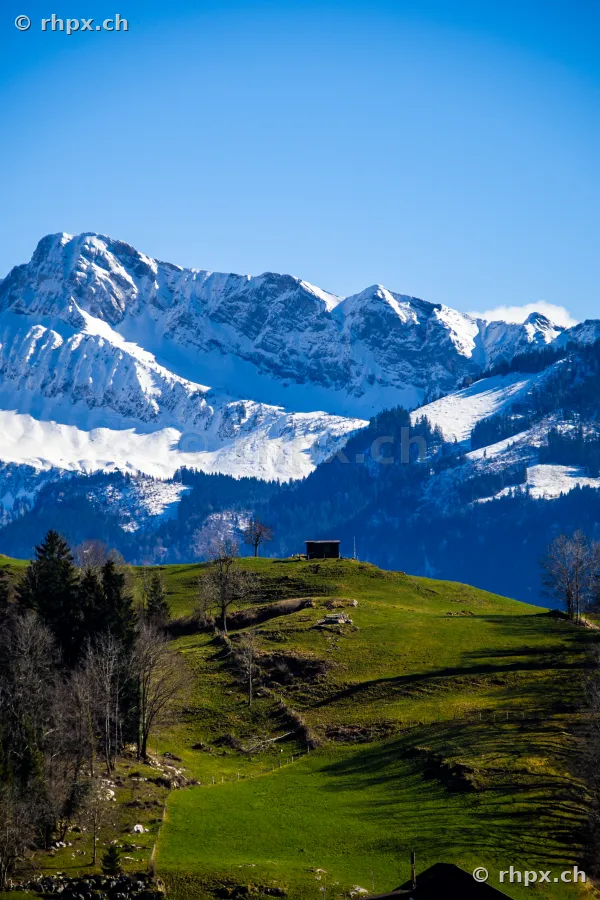 Eine kleine Hütte auf einer grünen Wiese mit schneebedeckten Bergen im Hintergrund