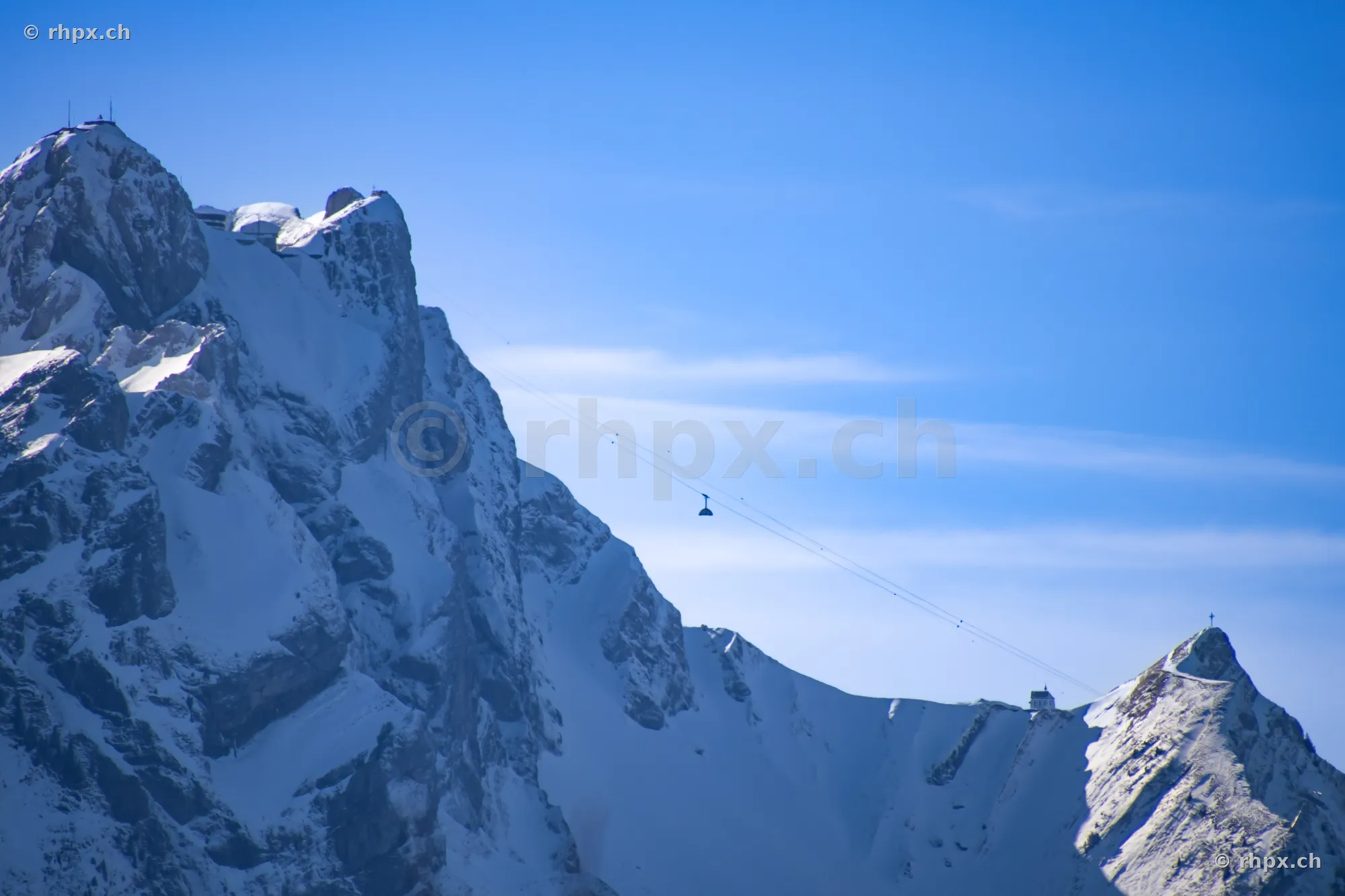 Blick auf die schneebedeckten Felswände des Pilatus mit einer Luftseilbahn vor blauem Himmel.